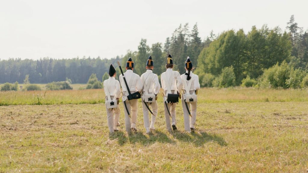 Group of reenactors in historical uniforms walking across a grassy field.