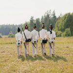Group of reenactors in historical uniforms walking across a grassy field.
